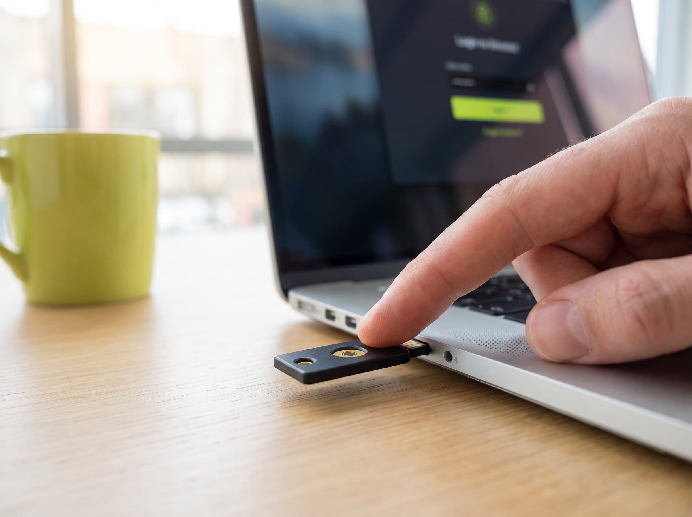 A hand inserting a security key (YubiKey) into a laptop showing a login screen